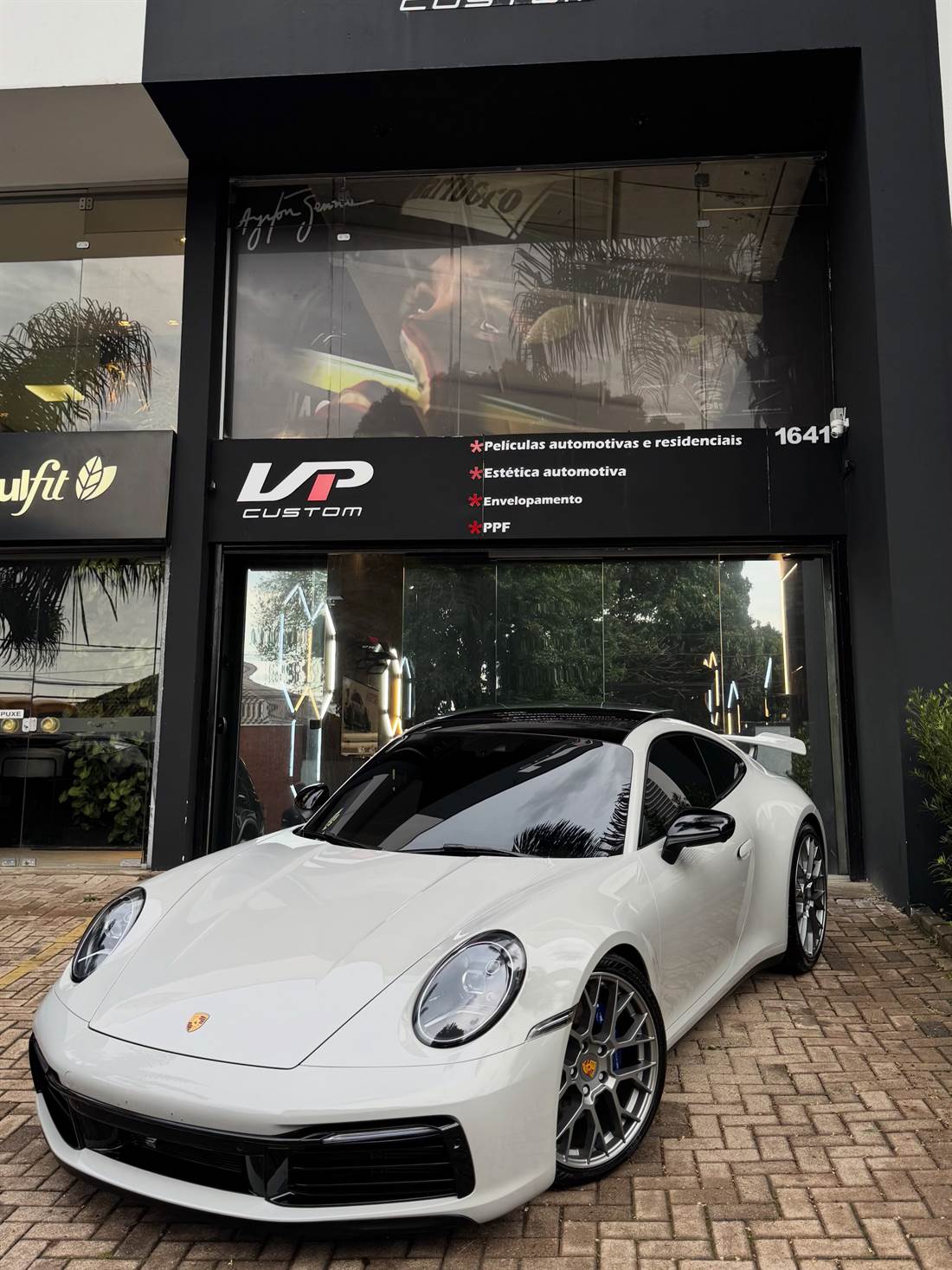 Porsche 911 branco em frente à fachada preta da VP Custom, com o letreiro de películas, estética automotiva, envelopamento e PPF